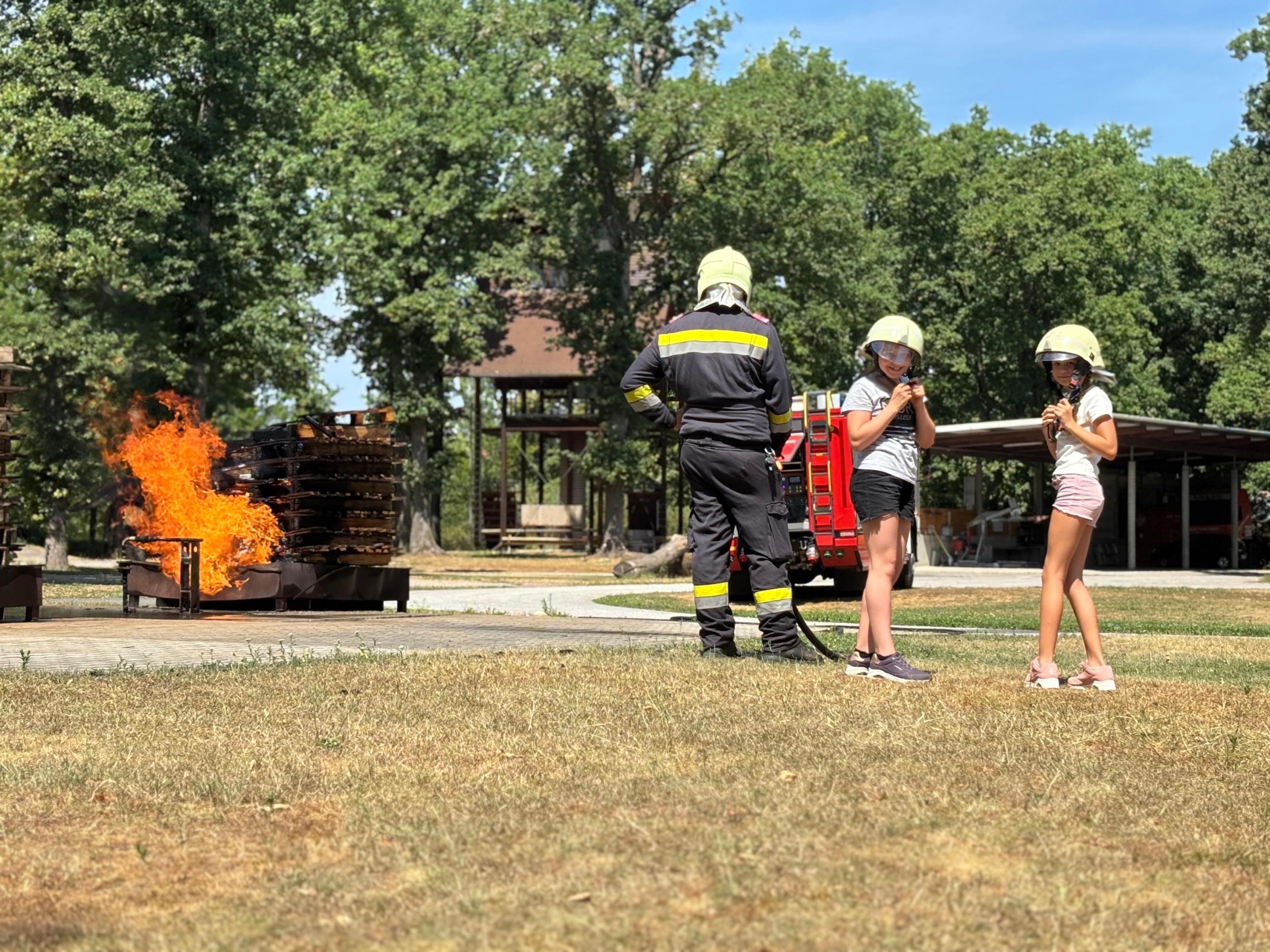 2 Mädchen mit Feuerwehrhelm neben einer Feuervorführung.